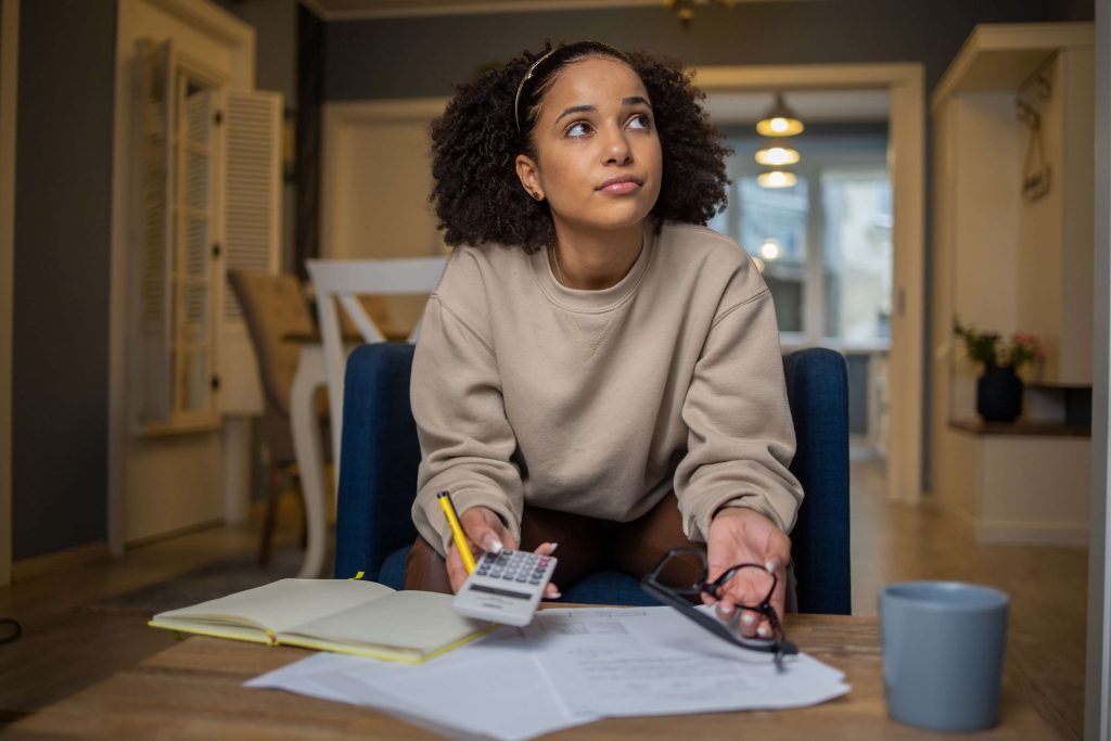 Woman sat at desk holding calculator, pen and glasses in her hands looking at bank letter