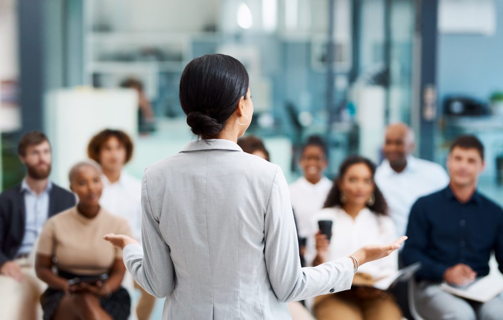 Businesswoman speaking to a team in an office setting, representing the importance of a key person in driving business success and why their protection matters