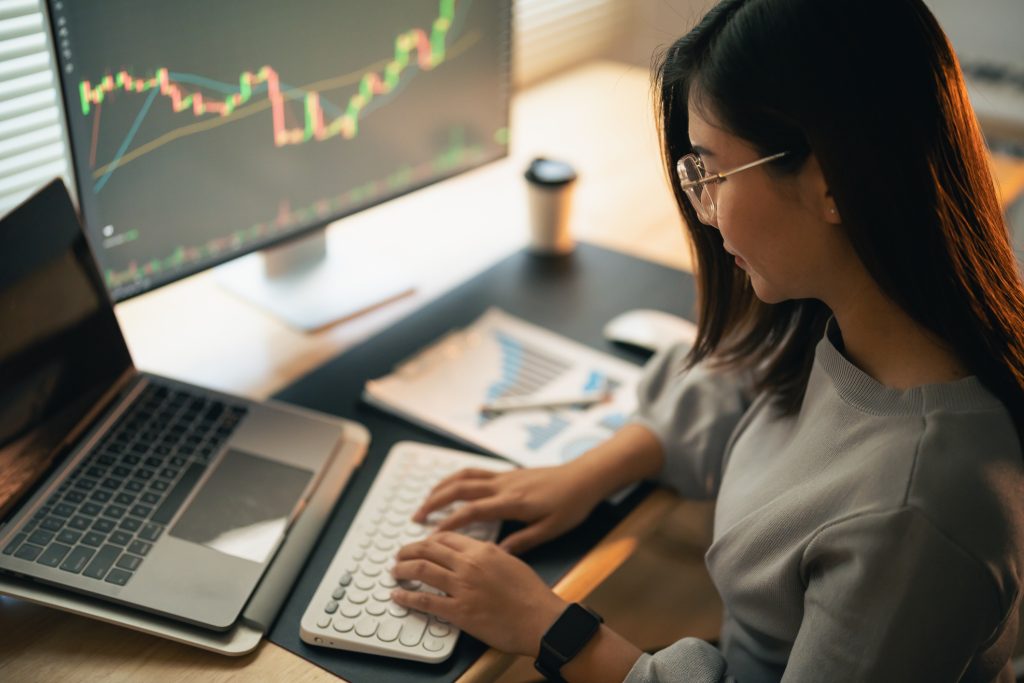 Asian Business Woman is checking Bitcoin or stock market price chart on the digital exchange on a laptop monitor computer, cryptocurrency future price action prediction.