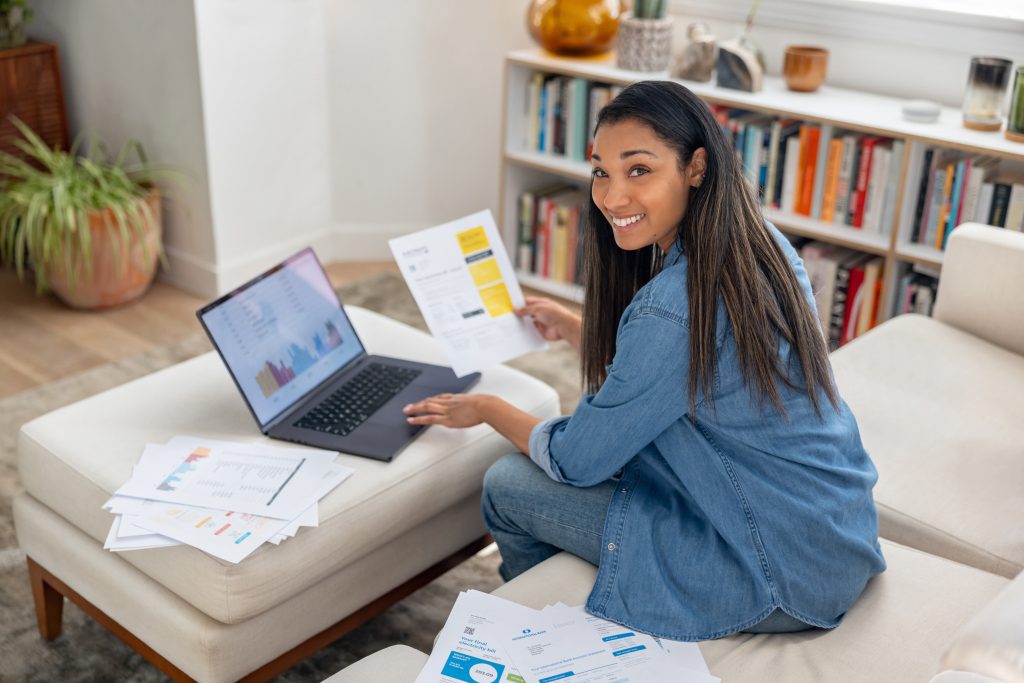 A woman at home on the sofa with a laptop and life insurance paperwork in front of her