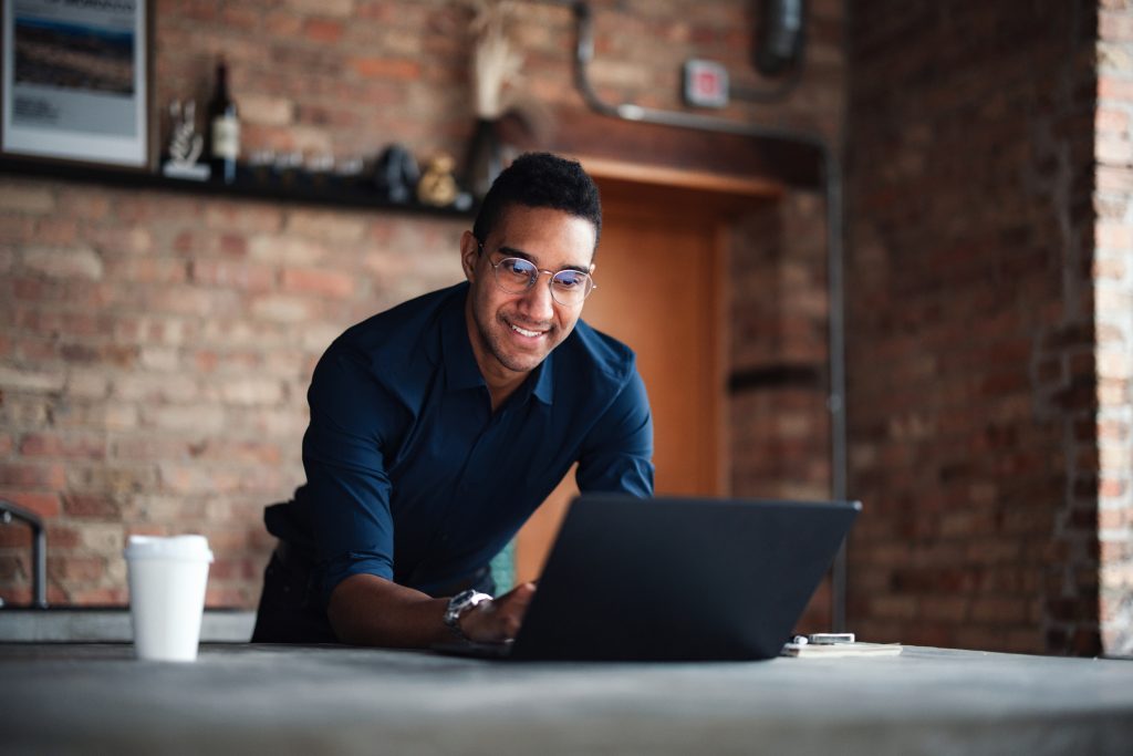A confident individual working on a laptop in a stylish, brick-walled office environment. The image conveys ambiance of productivity and focus.