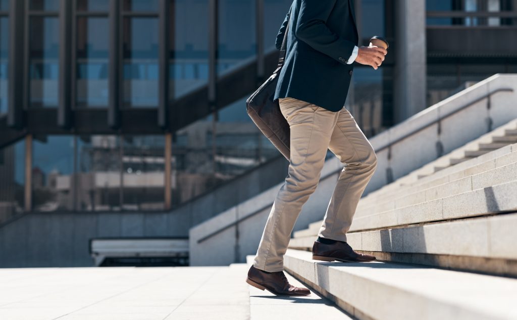 Shot of a businessman walking up a flight of stairs, returning to work after being sick, against an urban background