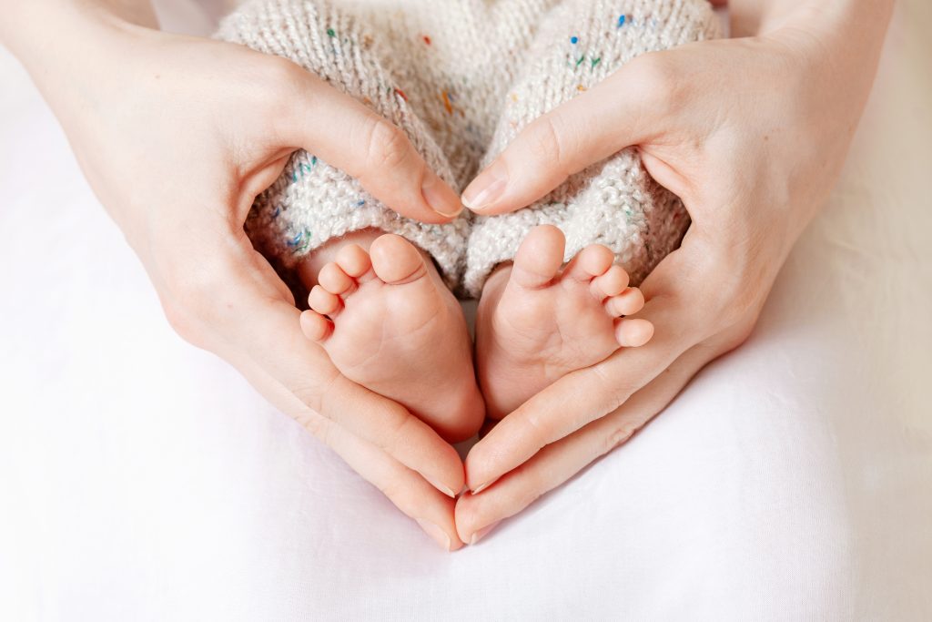 Baby feet in mother hands. Tiny Newborn Baby's feet on female Heart Shaped hands closeup.