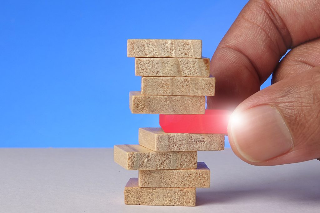 Risk or stability concept as male hand pulling red wooden block from a stack of wooden blocks.