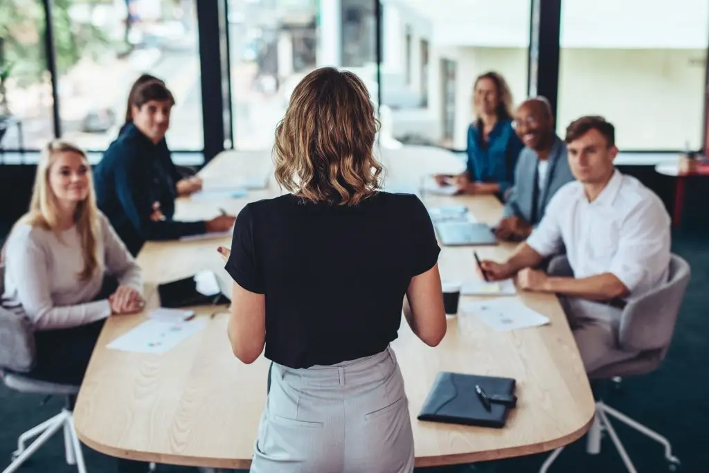 Rear view of a businesswoman addressing a meeting in office. Female business founder having a meeting with her team in office boardroom.