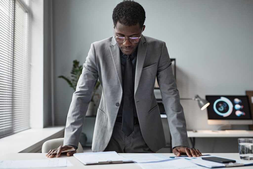 Portrait of successful businessman leaning over desk in office and reading document.